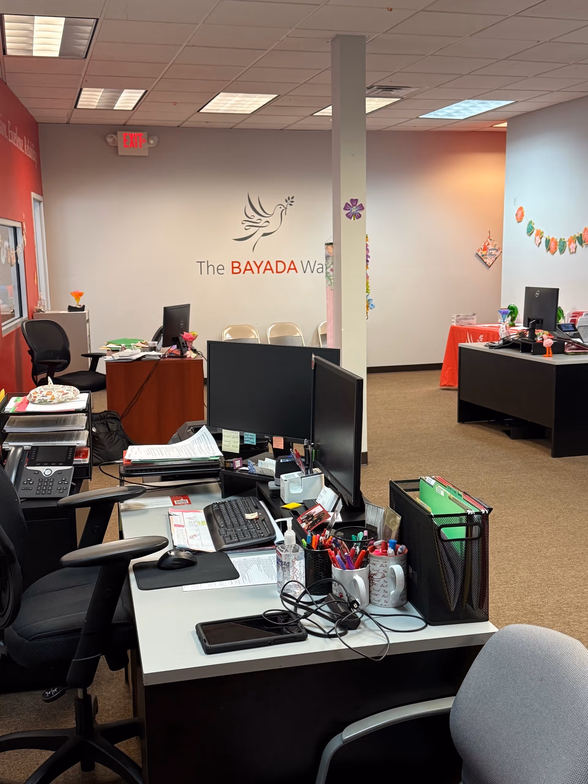 Office workspace with desks, computers, and BAYADA logo on the wall.