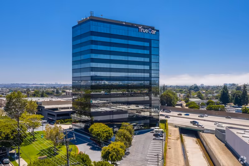 Tall glass office tower with a TrueCar sign amid highways and greenery.