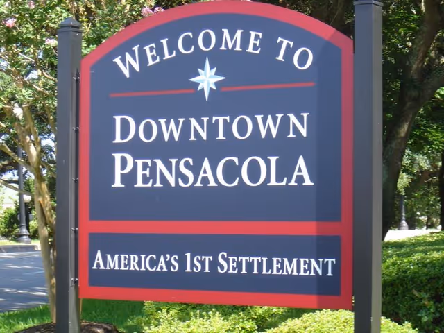 Outdoor welcome sign reading Downtown Pensacola with trees nearby.