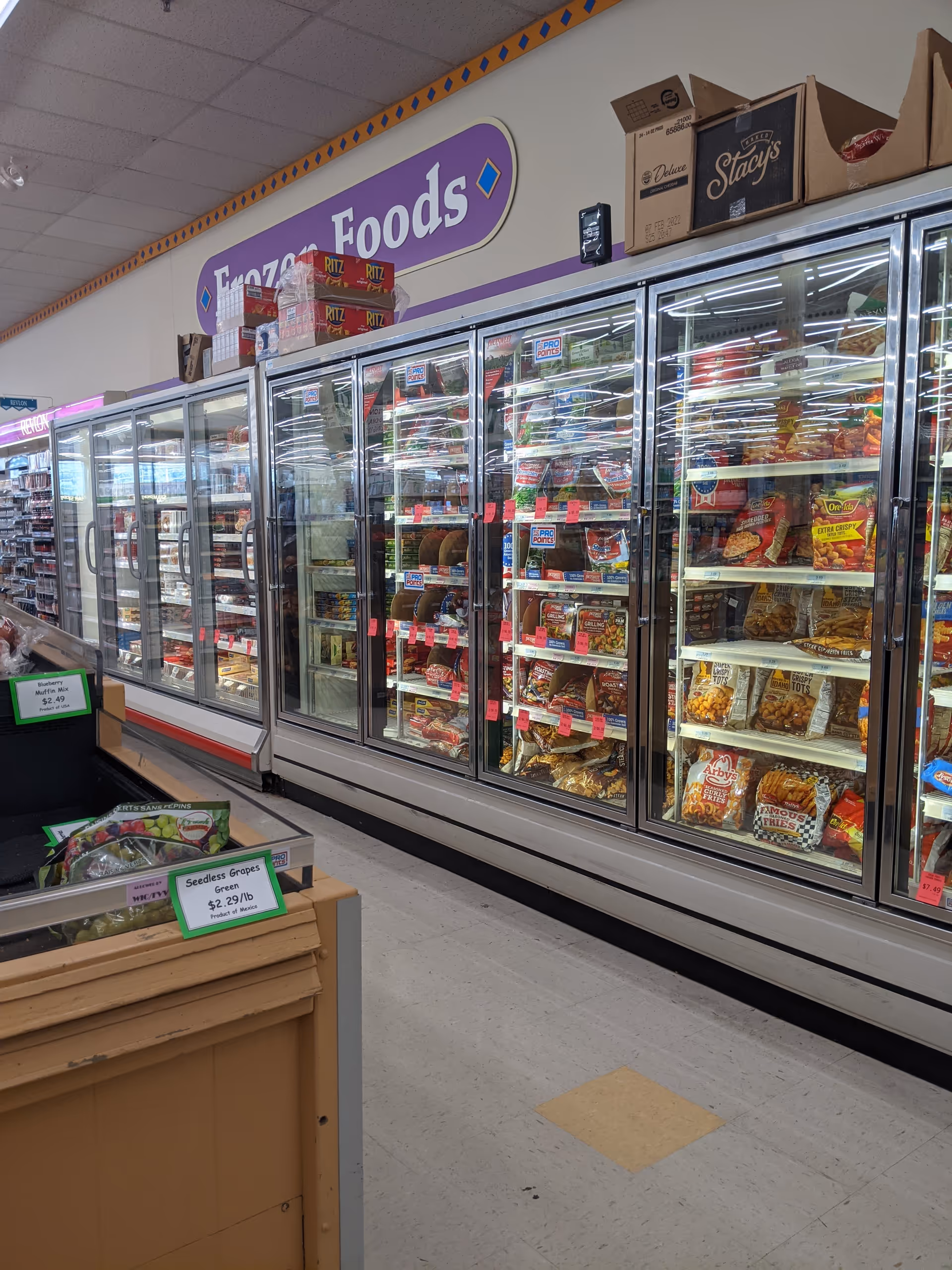 Inside a Discount Drug Mart, glass-door freezers line the aisle with assorted frozen foods.