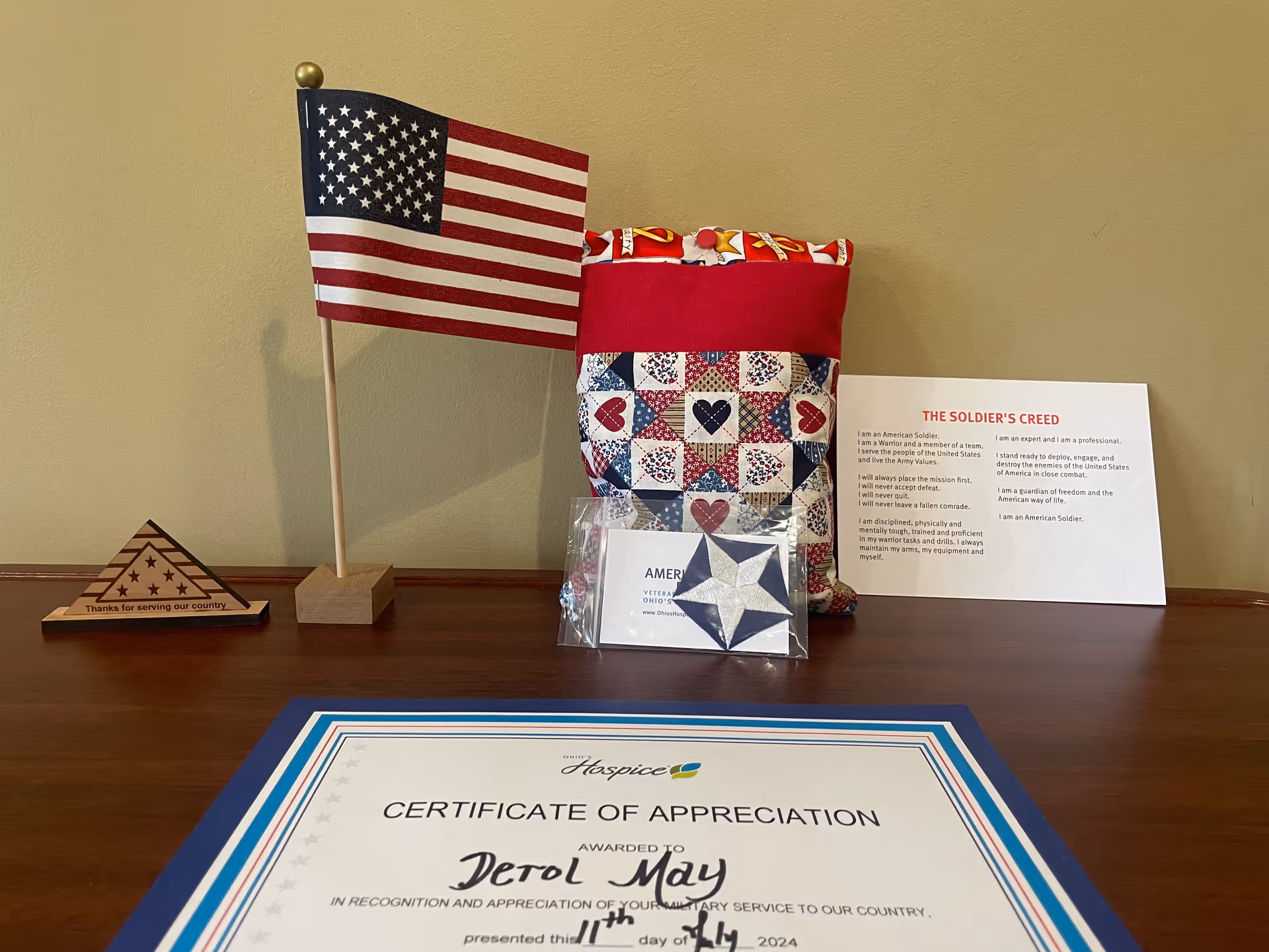 Patriotic display on a wooden table featuring American flag, quilted bag, and certificate.