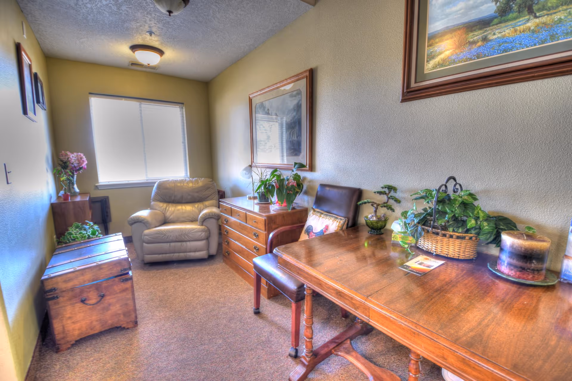 A cozy living room with a wooden desk, leather chair, plants, and framed art.