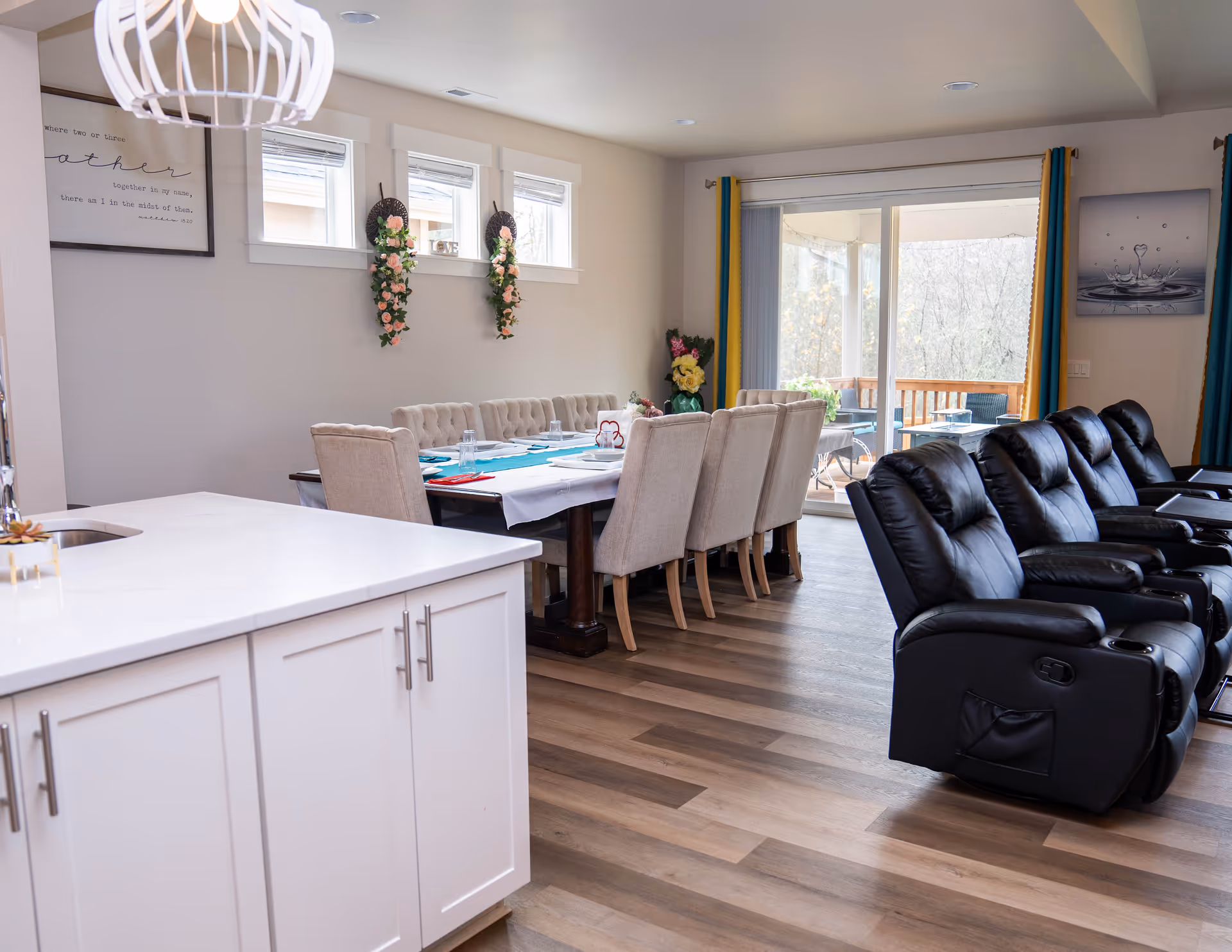 Bright dining area with long table, cream chairs, white island, and black recliners.