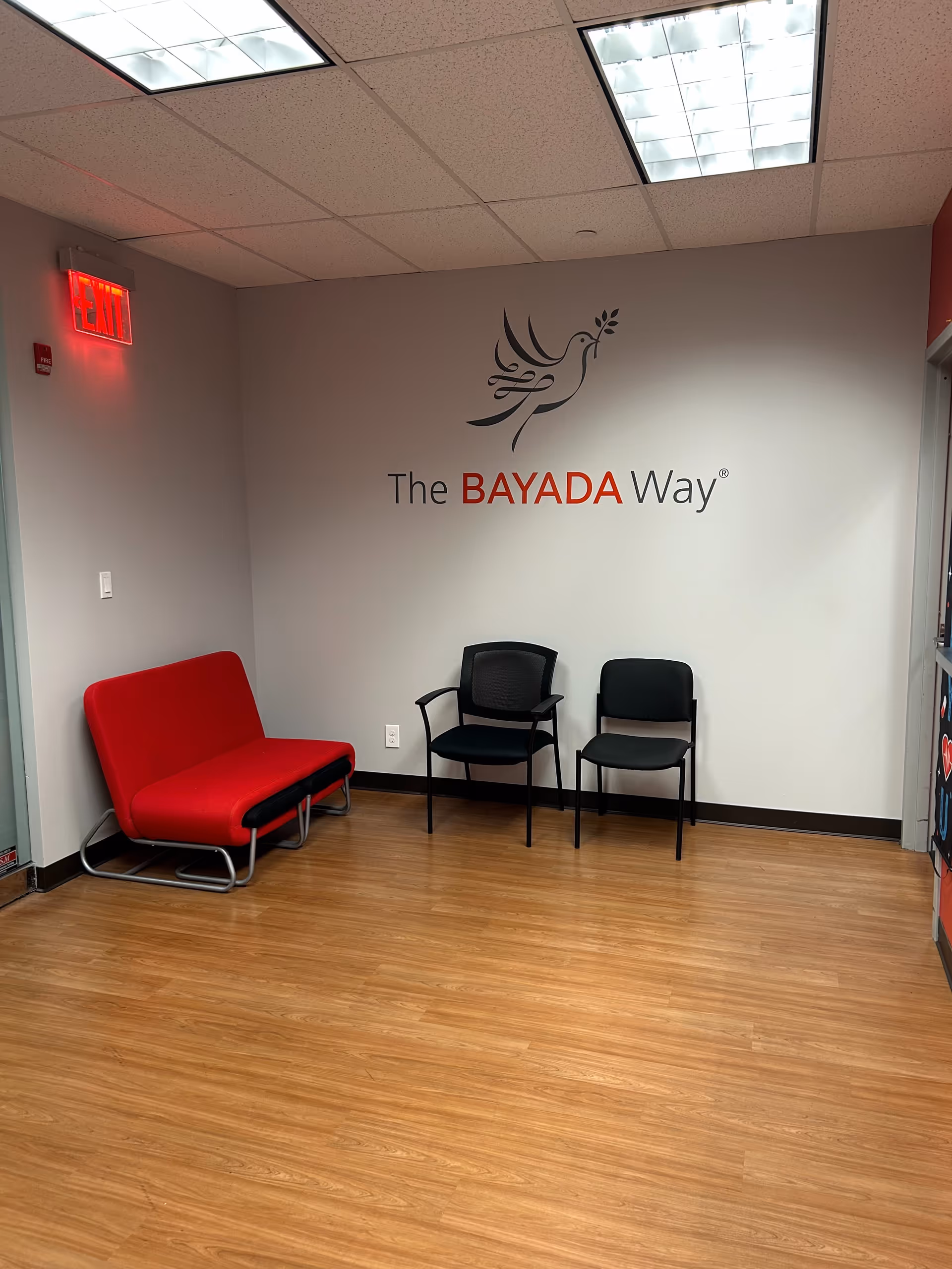 Indoor waiting area with red couch, black chairs, and The BAYADA Way logo.