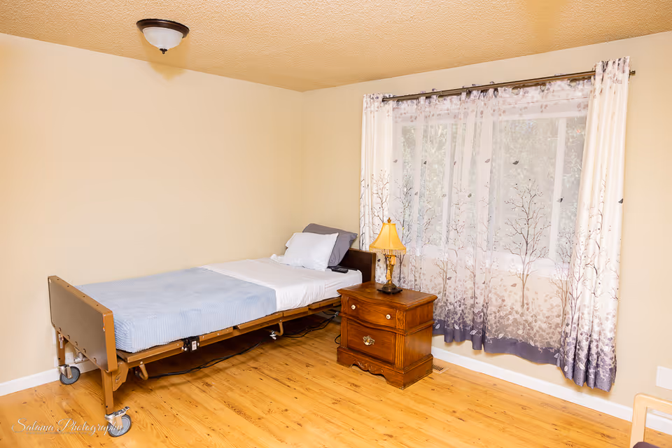 Single hospital bed with nightstand and patterned curtains in a bedroom.