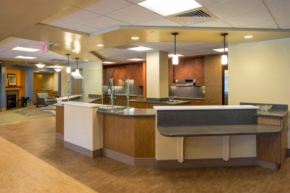 Interior kitchen area with curved service counters, glass dividers, and wood cabinets in a communal space.