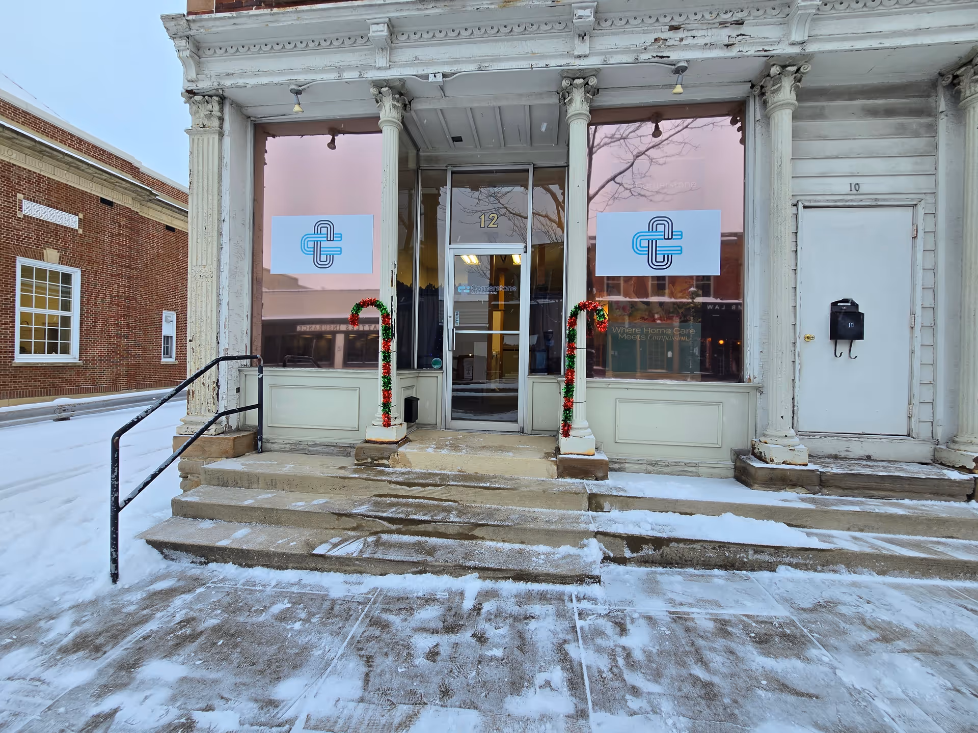 Snowy storefront entrance with glass doors, decorative garlands on columns, and signage for Cornerstone Caregiving.
