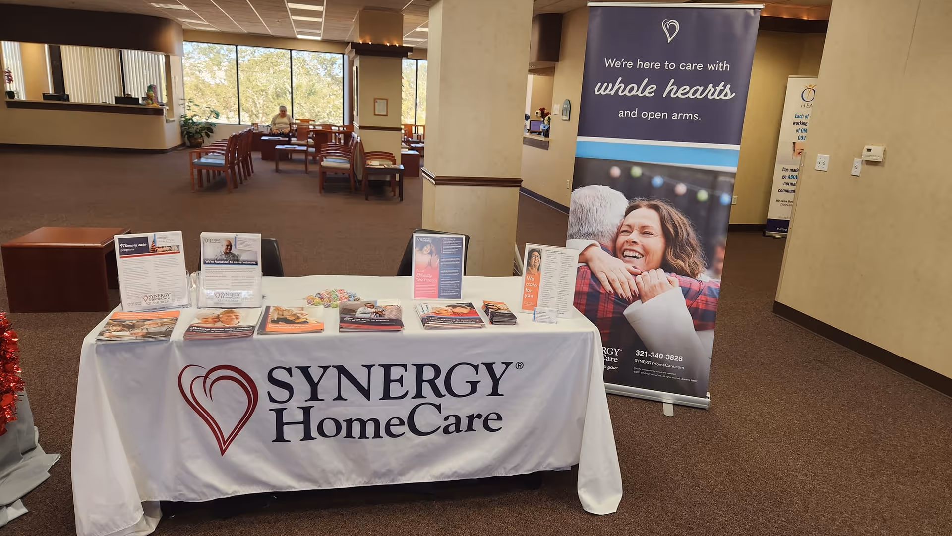 Promotional table with SYNERGY HomeCare branding in a spacious facility lobby.