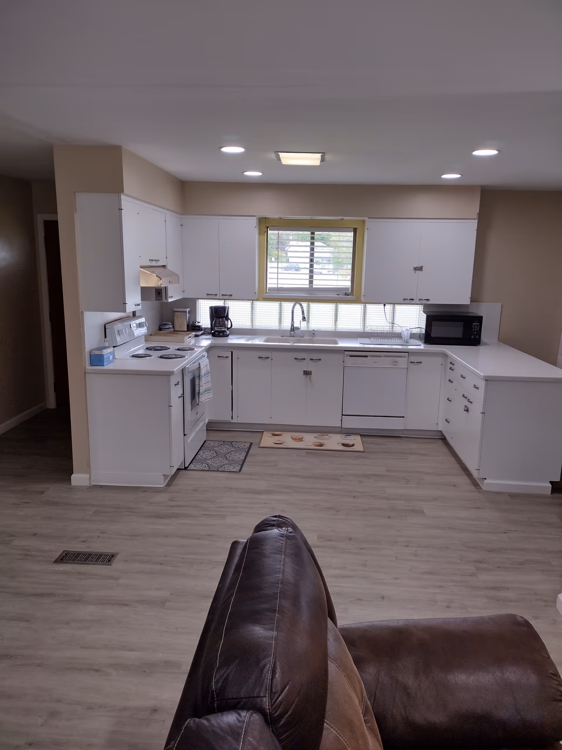 White kitchen with cabinets, appliances, and sink; a brown leather couch in foreground.