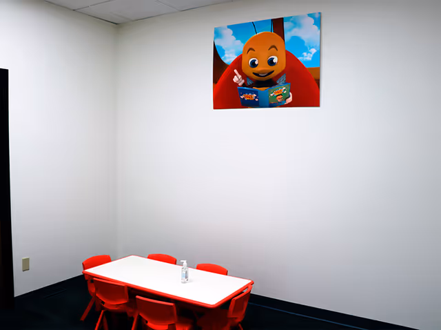 Small red table and chairs in a bright, plain room with a cartoon poster.
