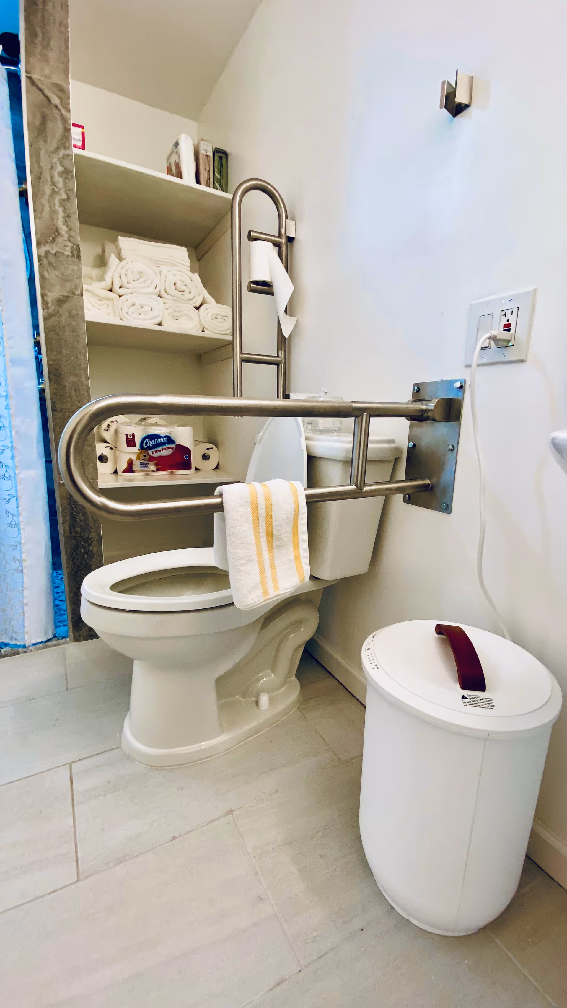 Accessible bathroom featuring a toilet with grab bars, towel rack, and towel shelves.