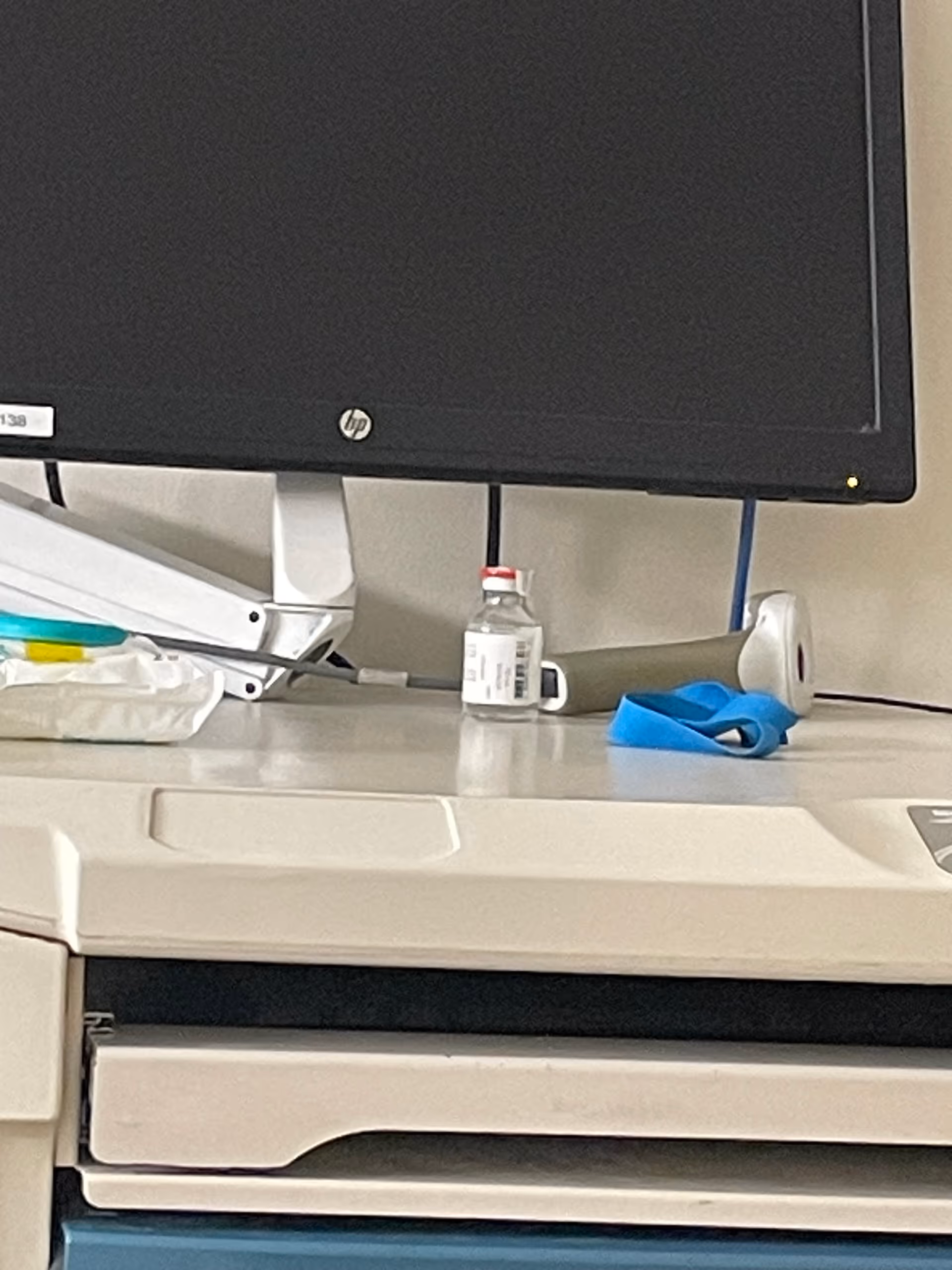 Close-up of a desk with a computer monitor, a small vial, and a blue glove.