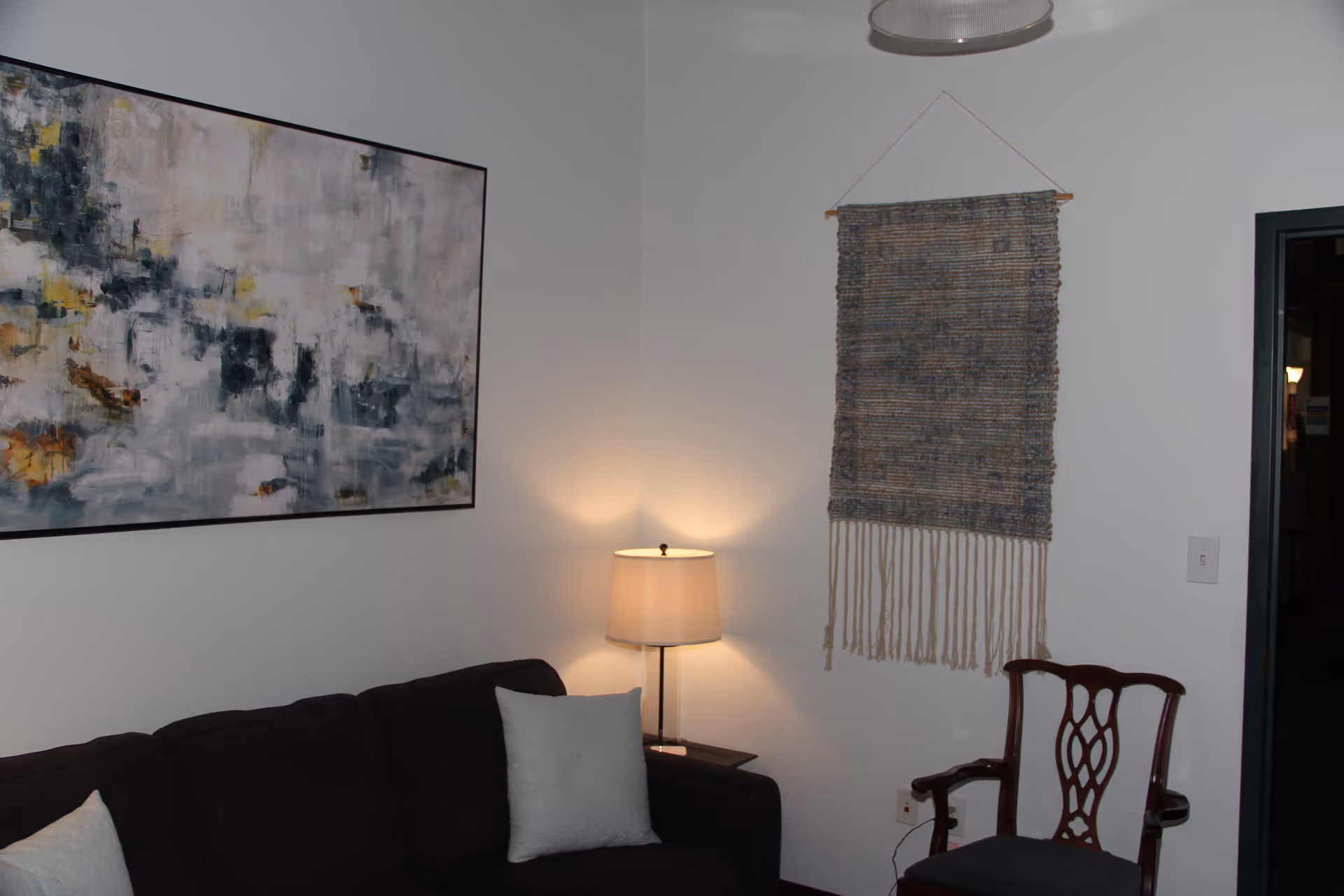 Cozy living room with sofa, lamp, wall art, and a woven hanging.