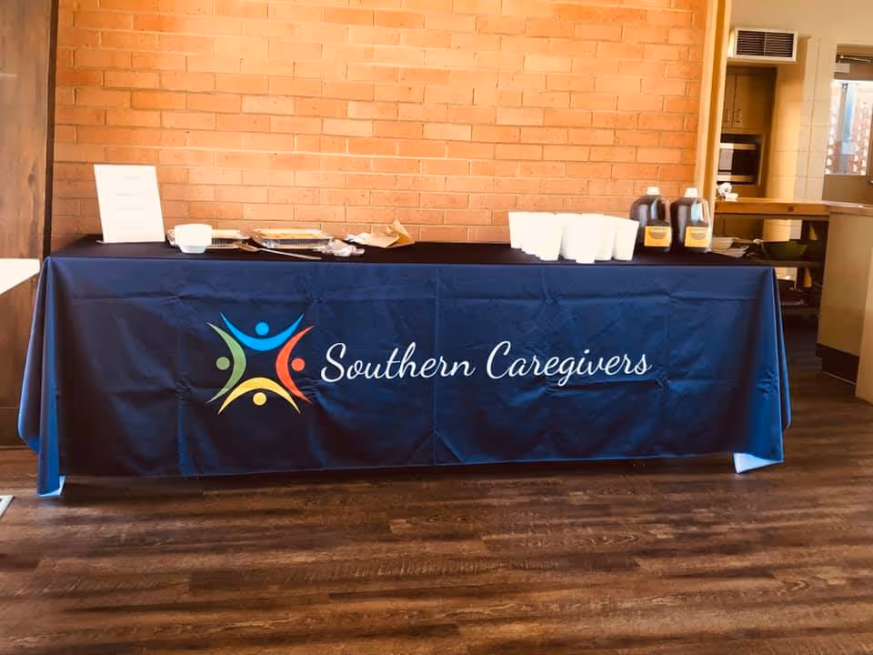 Indoor reception table with a blue Southern Caregivers banner and disposable cups.