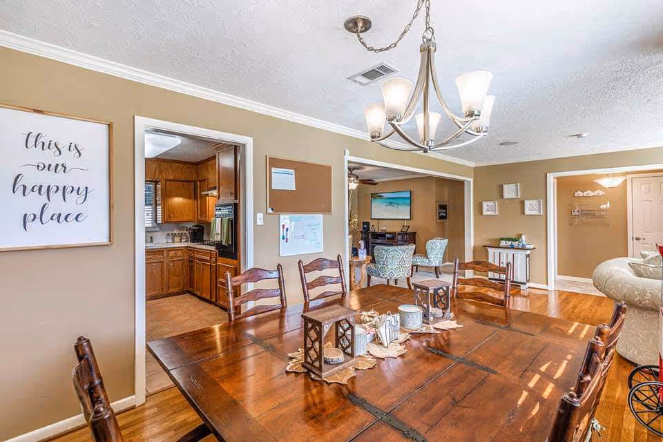 Open dining area with a wooden table, chandelier, and adjacent living and kitchen spaces.