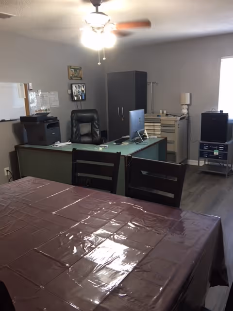 Office area with desk, chair, filing cabinet, computer, and covered table.