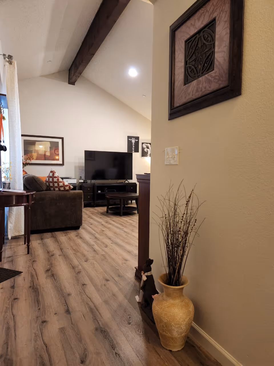 Interior living room with a brown sofa, TV stand, wood floor, and decorative vase.