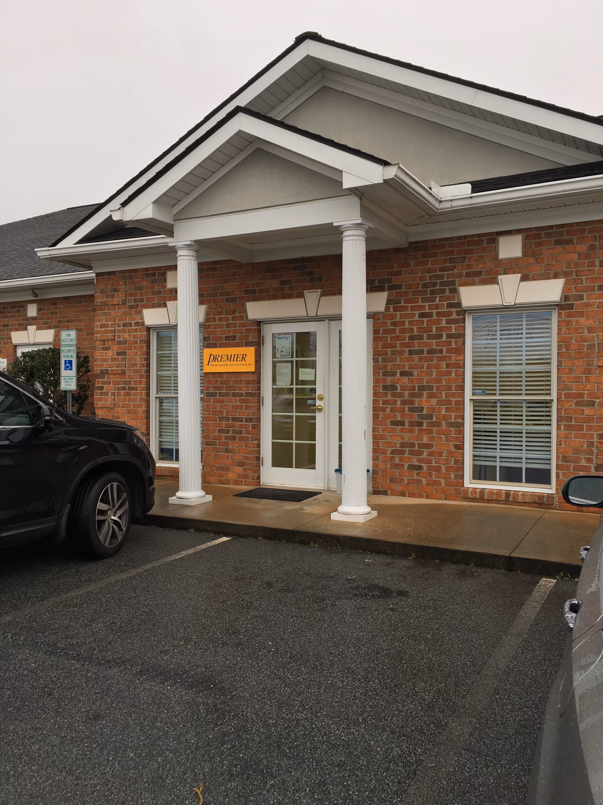 Brick facility entrance with white columns, glass doors, Premier sign, and adjacent parking.