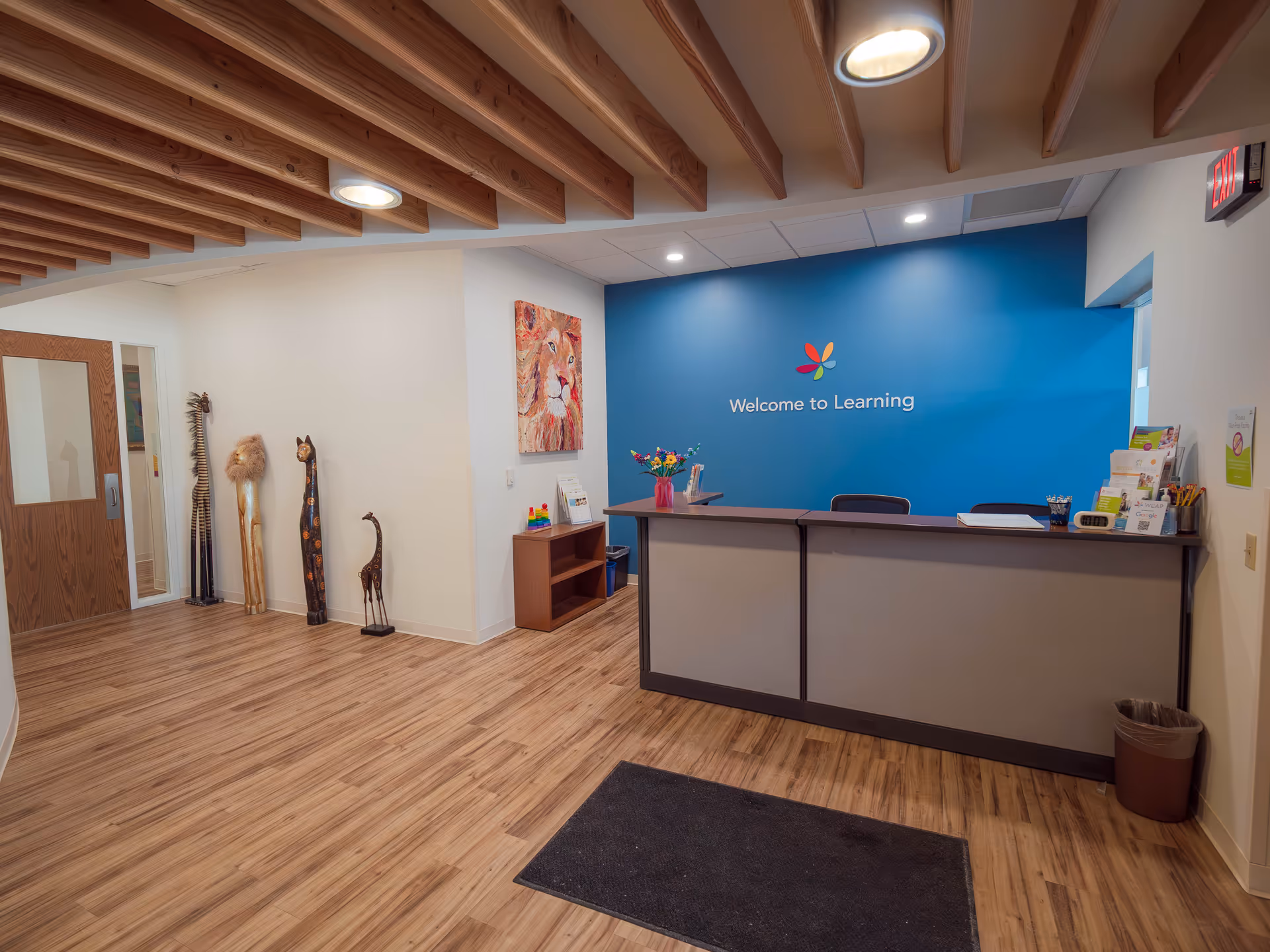 Reception area with a blue wall reading 'Welcome to Learning,' wooden floor, and decorative giraffe statues.