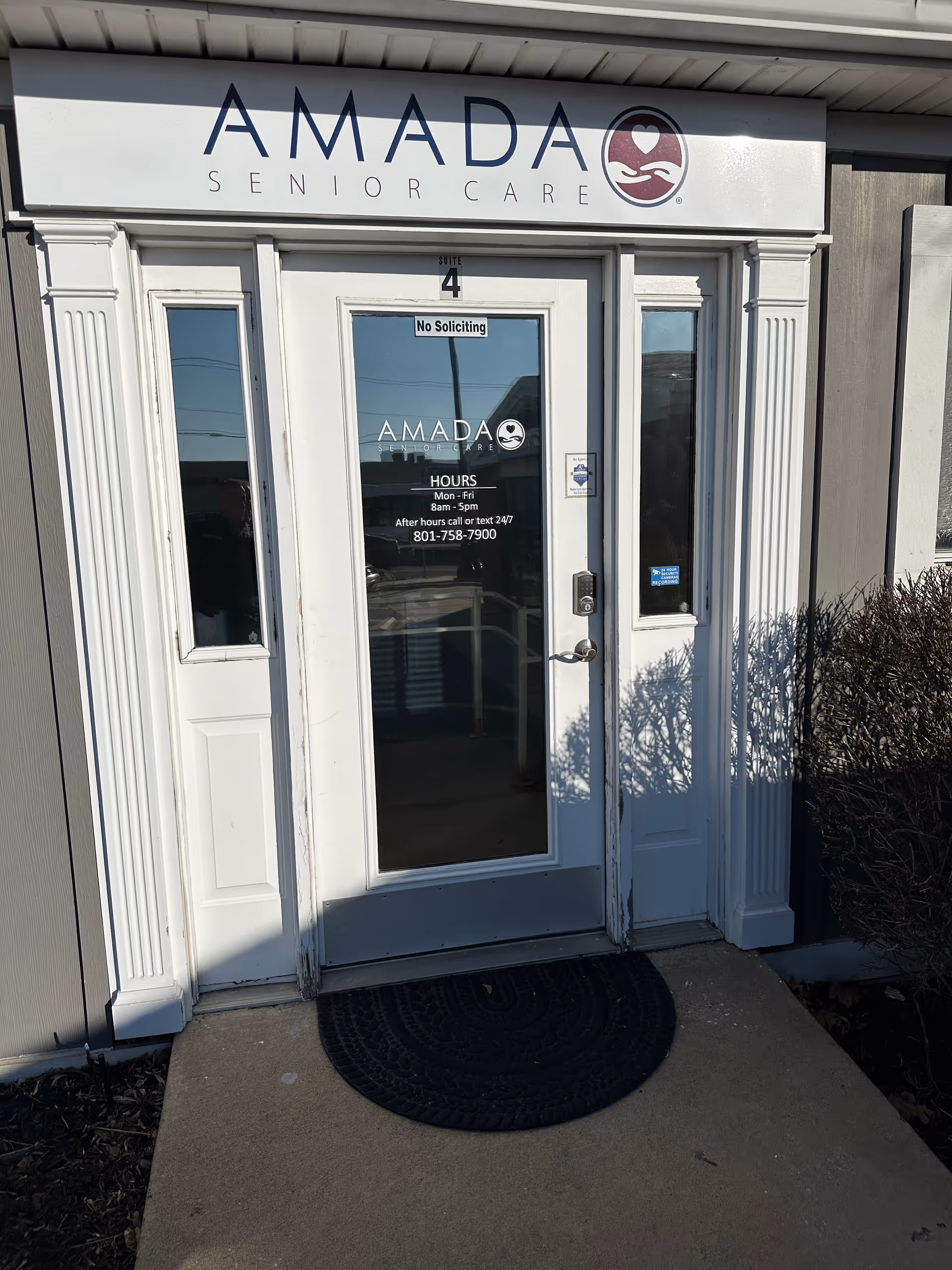 Exterior entrance of Amada Senior Care with a glass door and sign above.