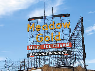 Tall metal billboard frame displaying Meadow Gold Milk Ice Cream over a brick building.