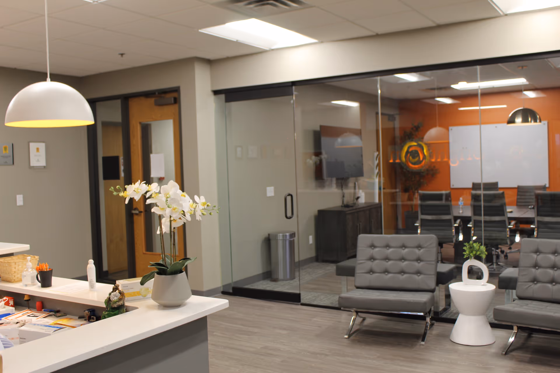 Modern reception and waiting area with glass walls, gray chairs, and a white reception desk.
