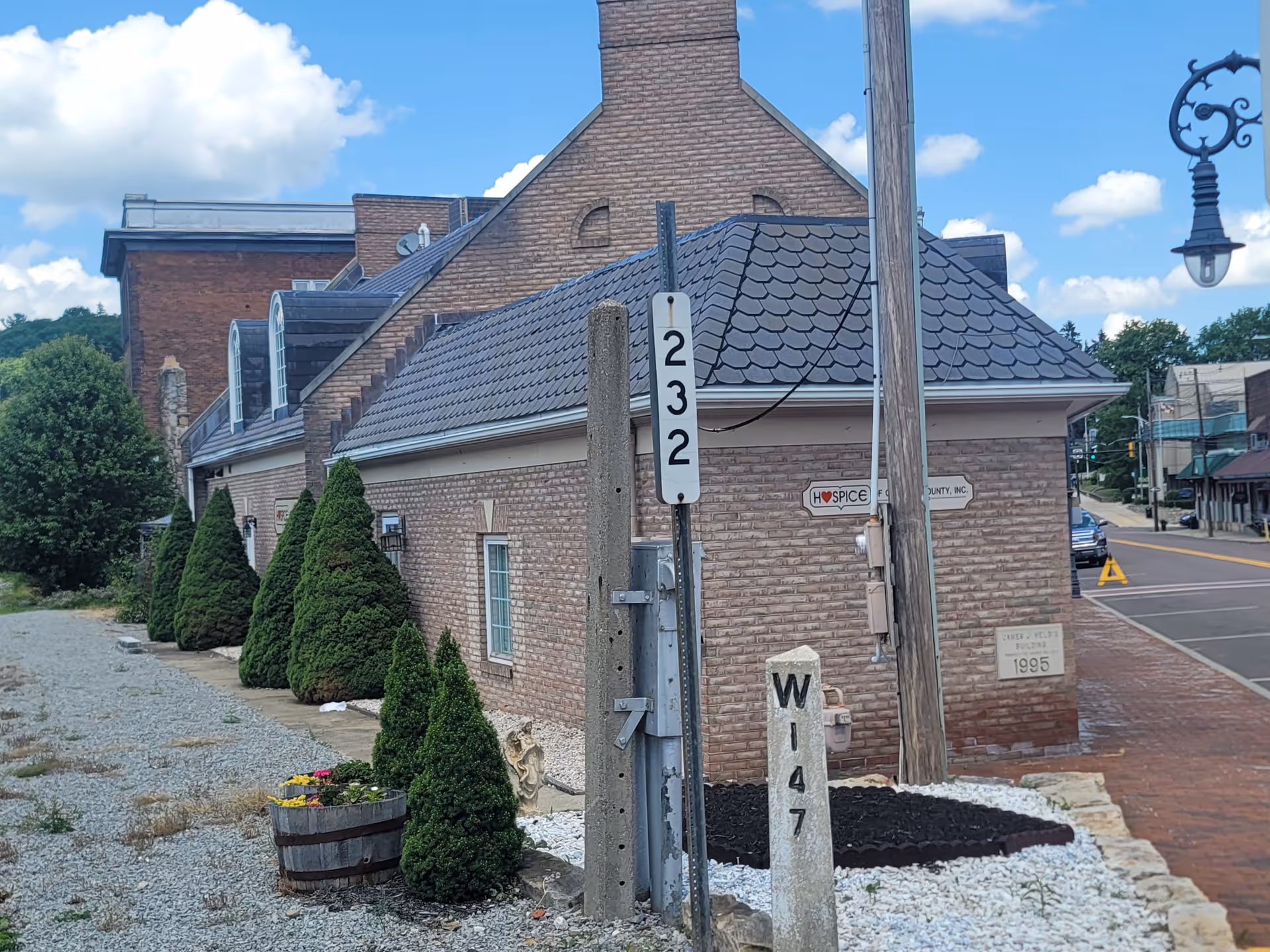 Brick hospice building along a street with trees, signs, and a utility pole.