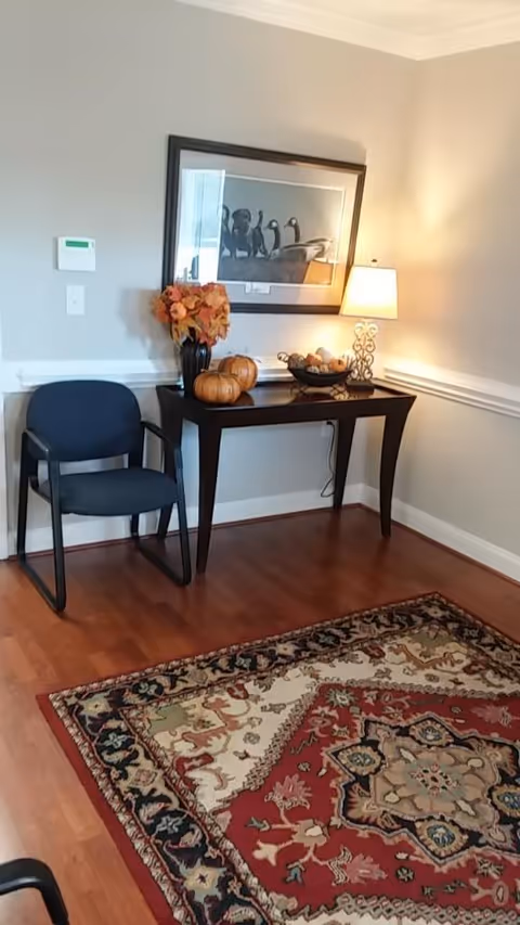 A console table, chair, lamp, pumpkins, flowers, and a framed photo in a softly lit corner.