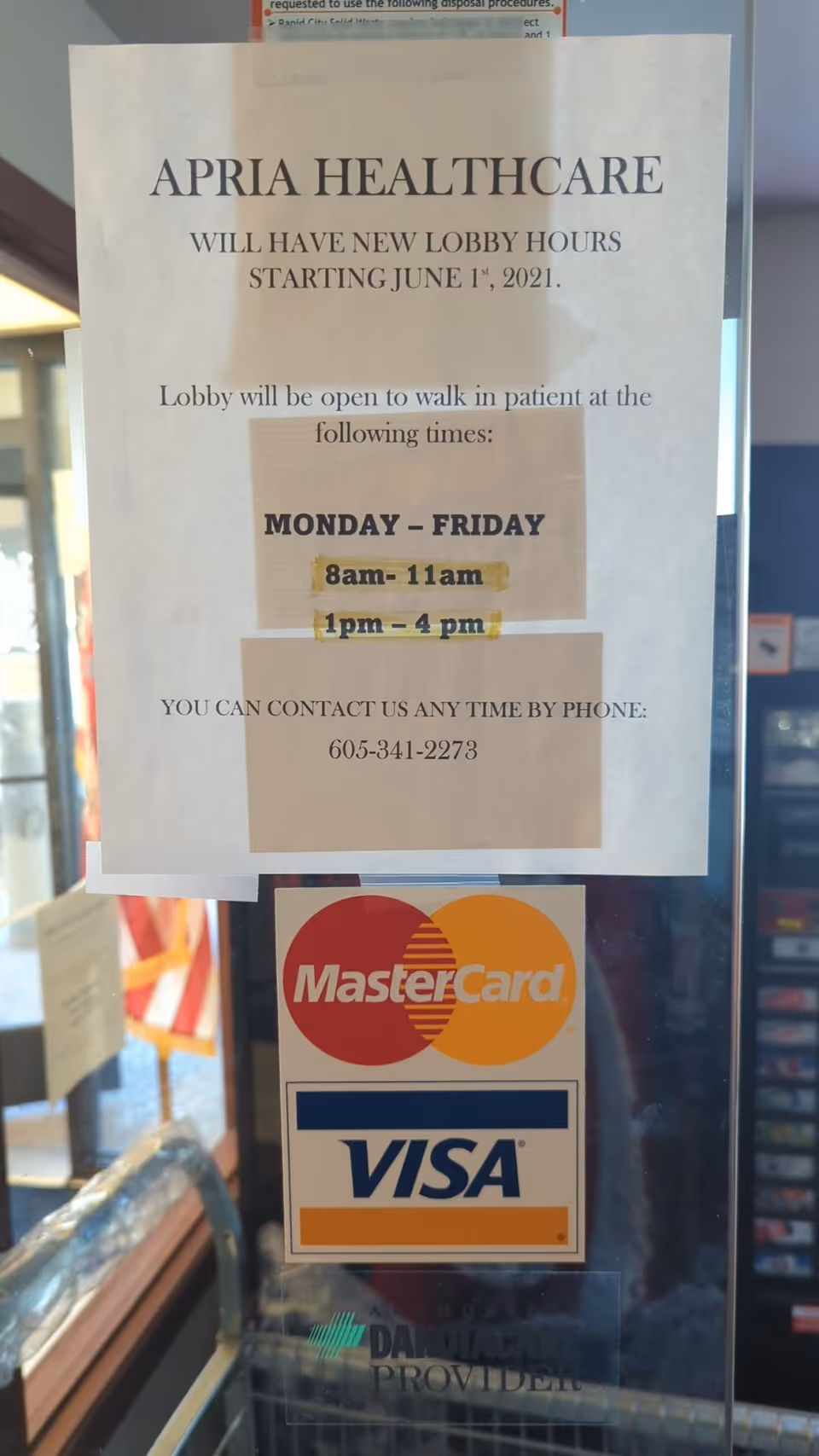 Apria Healthcare lobby hours poster on glass door with MasterCard and Visa logos.
