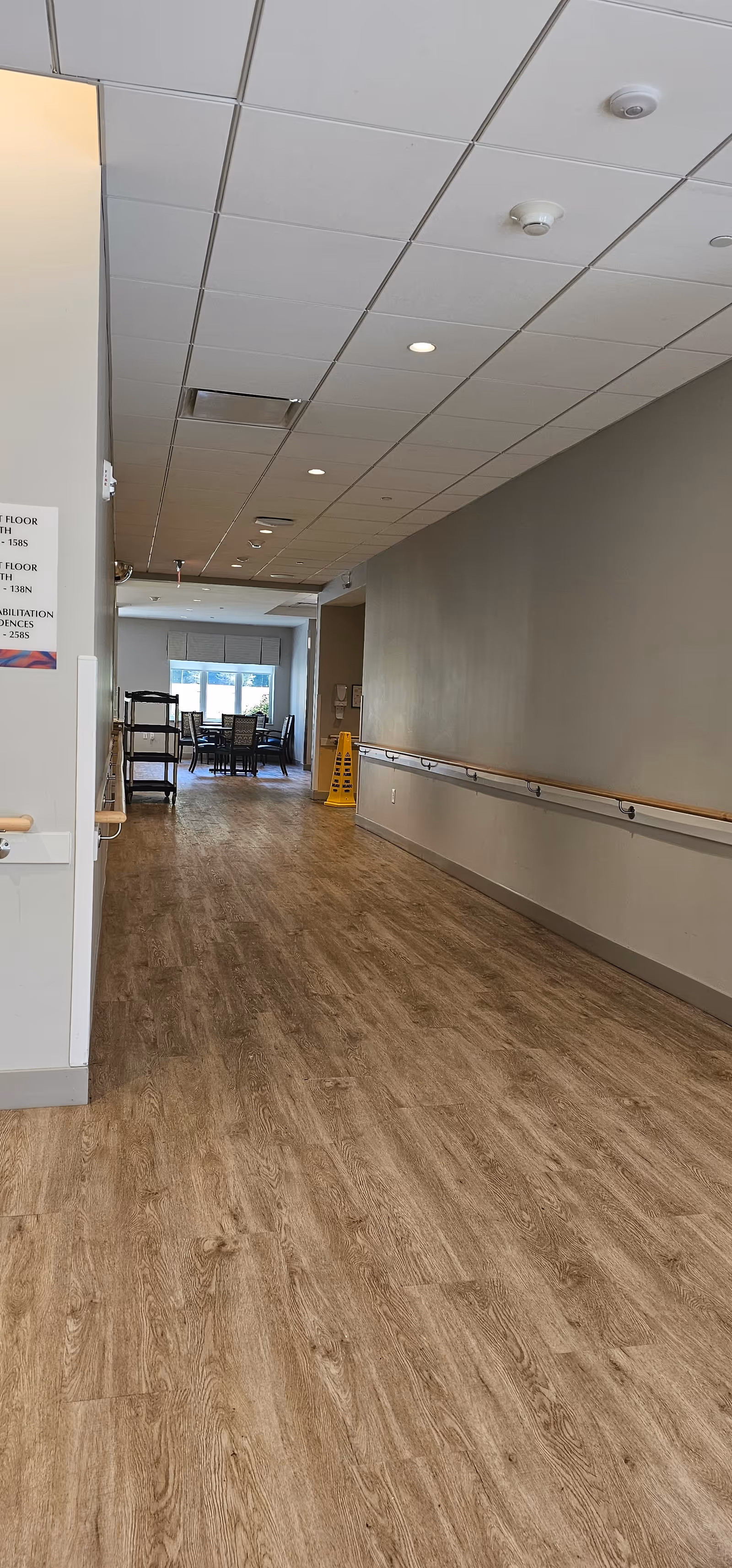 Long hallway inside a senior living facility with wood-like flooring and distant seating.