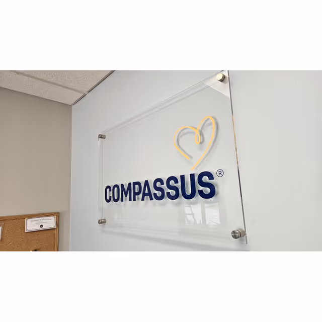 Interior wall sign reading Compassus with yellow heart logo.
