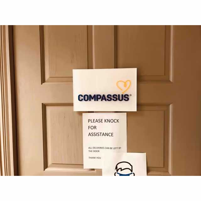 Door with Compassus sign and notice asking visitors to knock for assistance.