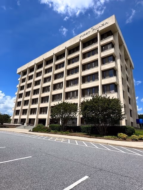 Tall beige multi-story senior living building with many windows and surrounding trees.