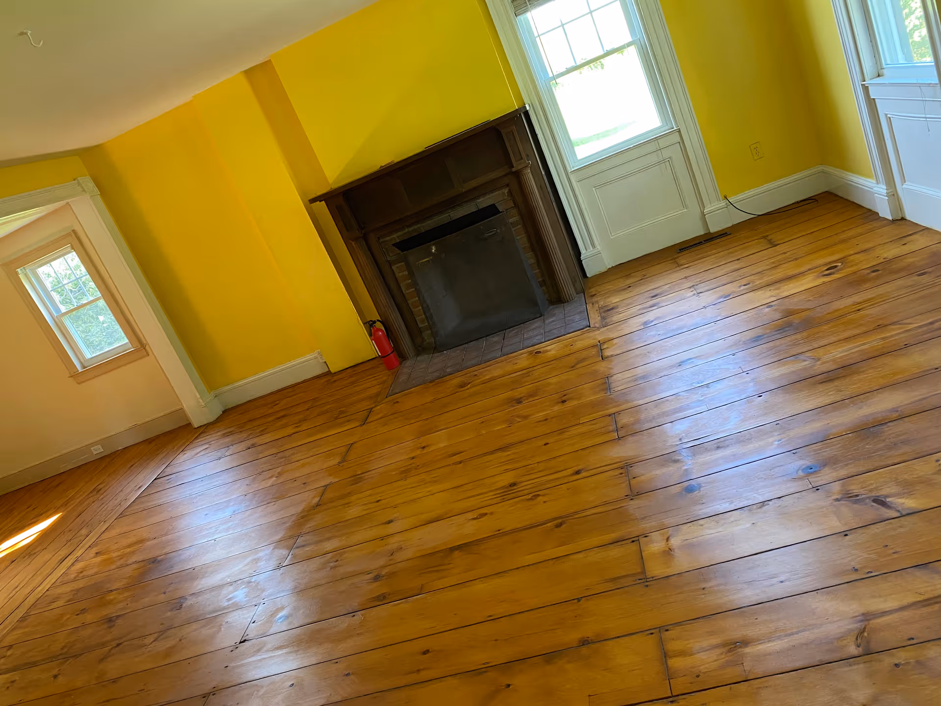 Bright yellow-walled room with wooden floor and a fireplace.
