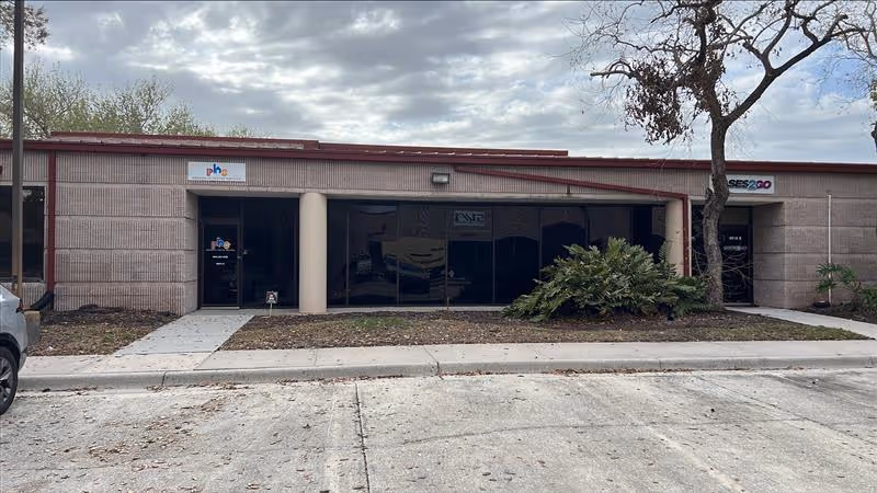 A single-story commercial building with glass storefronts and a concrete sidewalk.
