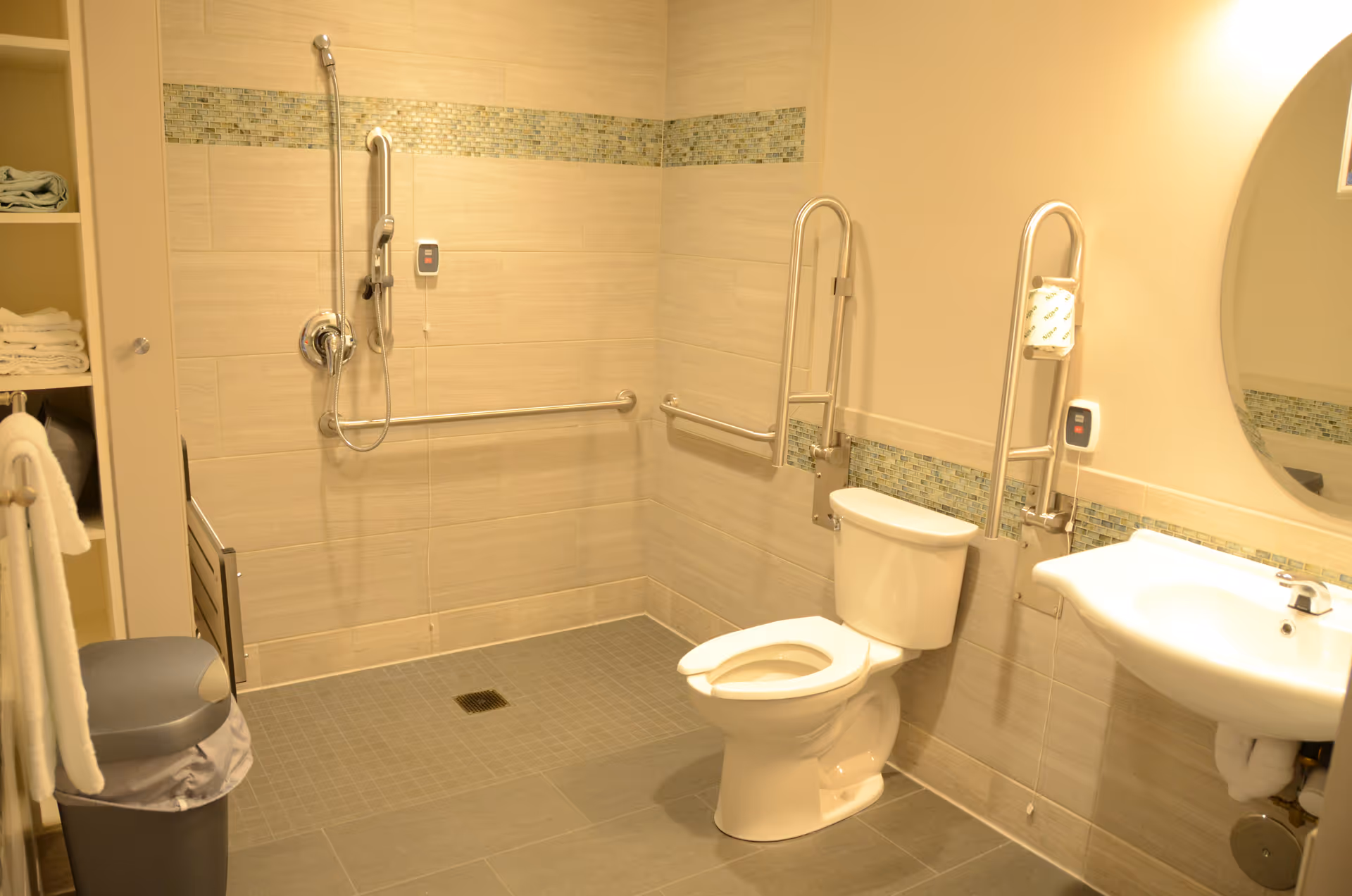 Accessible hospital-style bathroom with toilet, sink, mirror, and multiple grab bars.