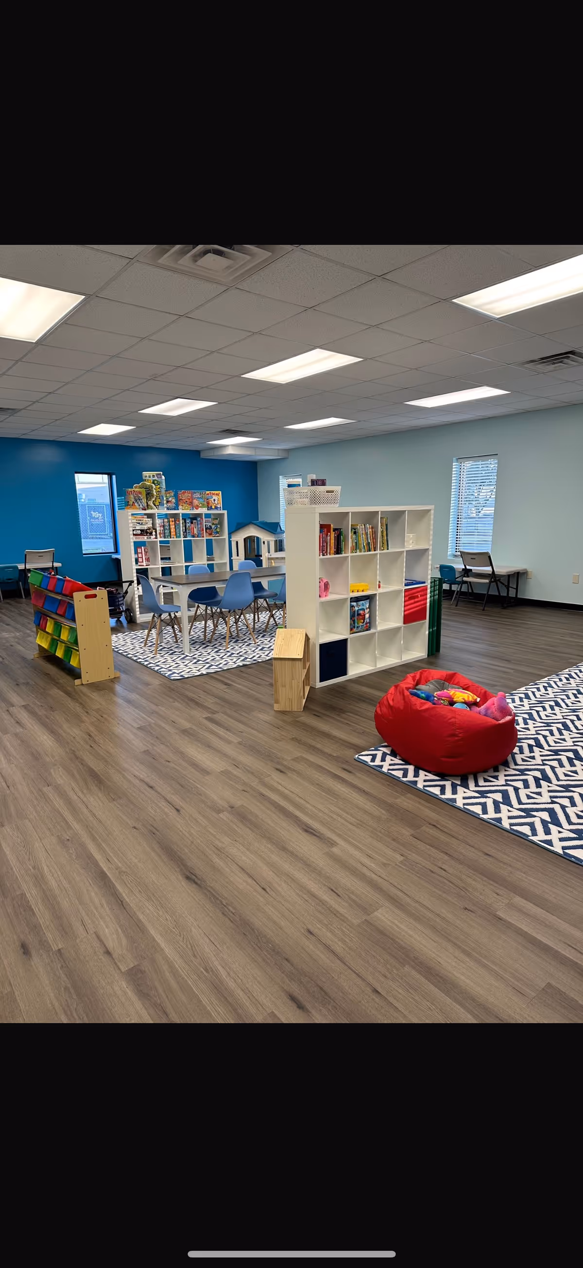 Bright senior living facility playroom with shelves, tables, chairs, and a red bean bag.