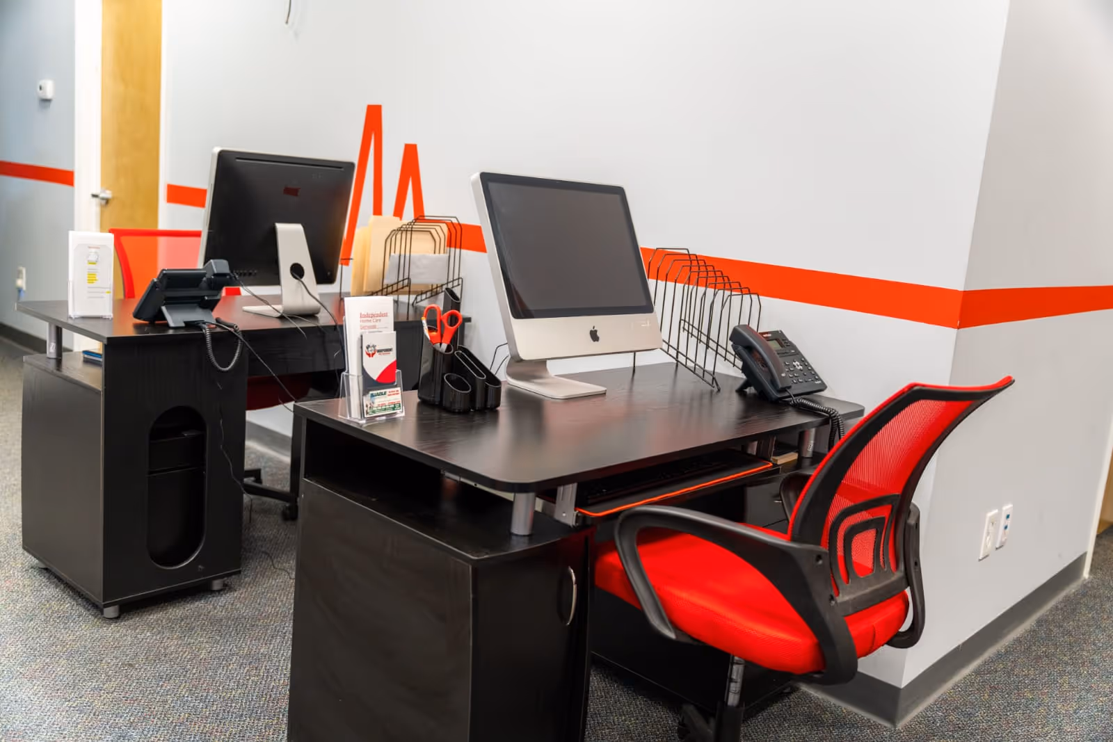 There is an office desk with computers and a red chair inside a facility.