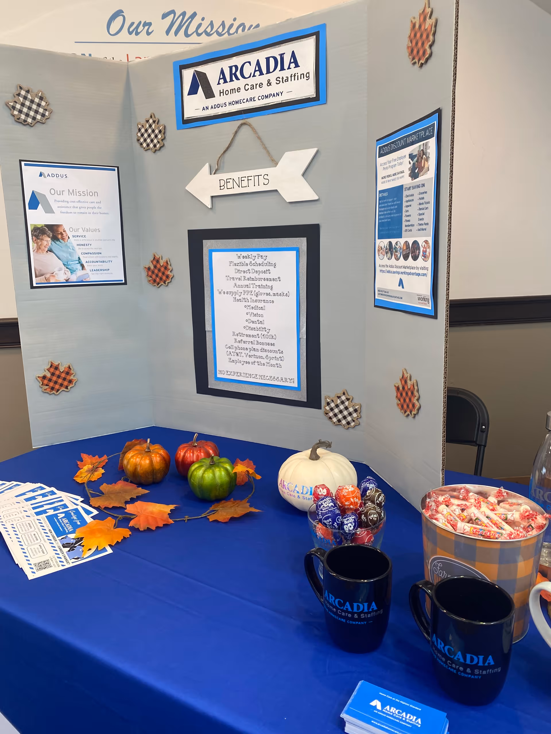 Indoor display booth with Arcadia Home Care and Staffing signage, pumpkins, candy, and cups.