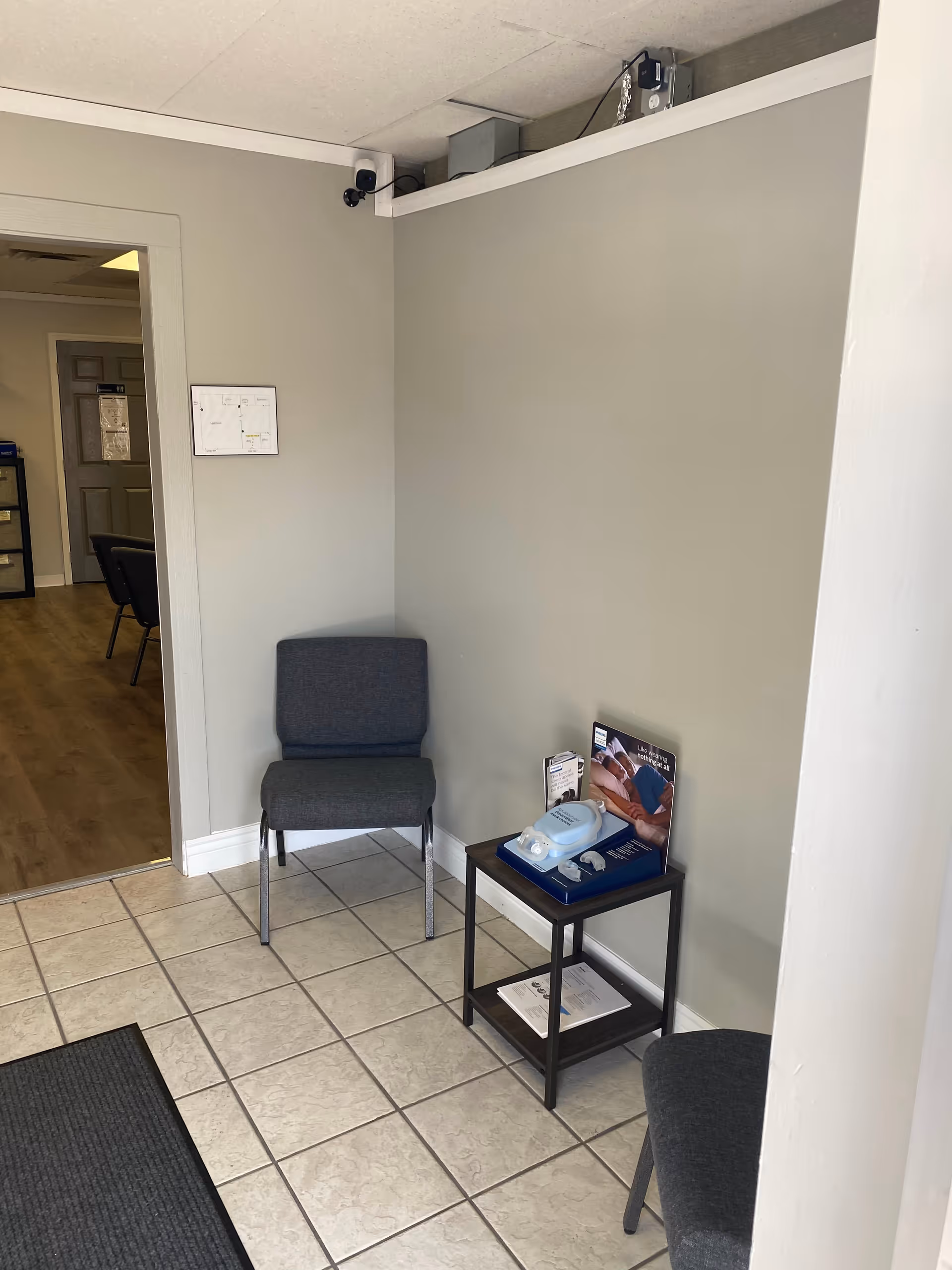 Corner waiting area with two gray chairs, a table of brochures, and entryway to another room.