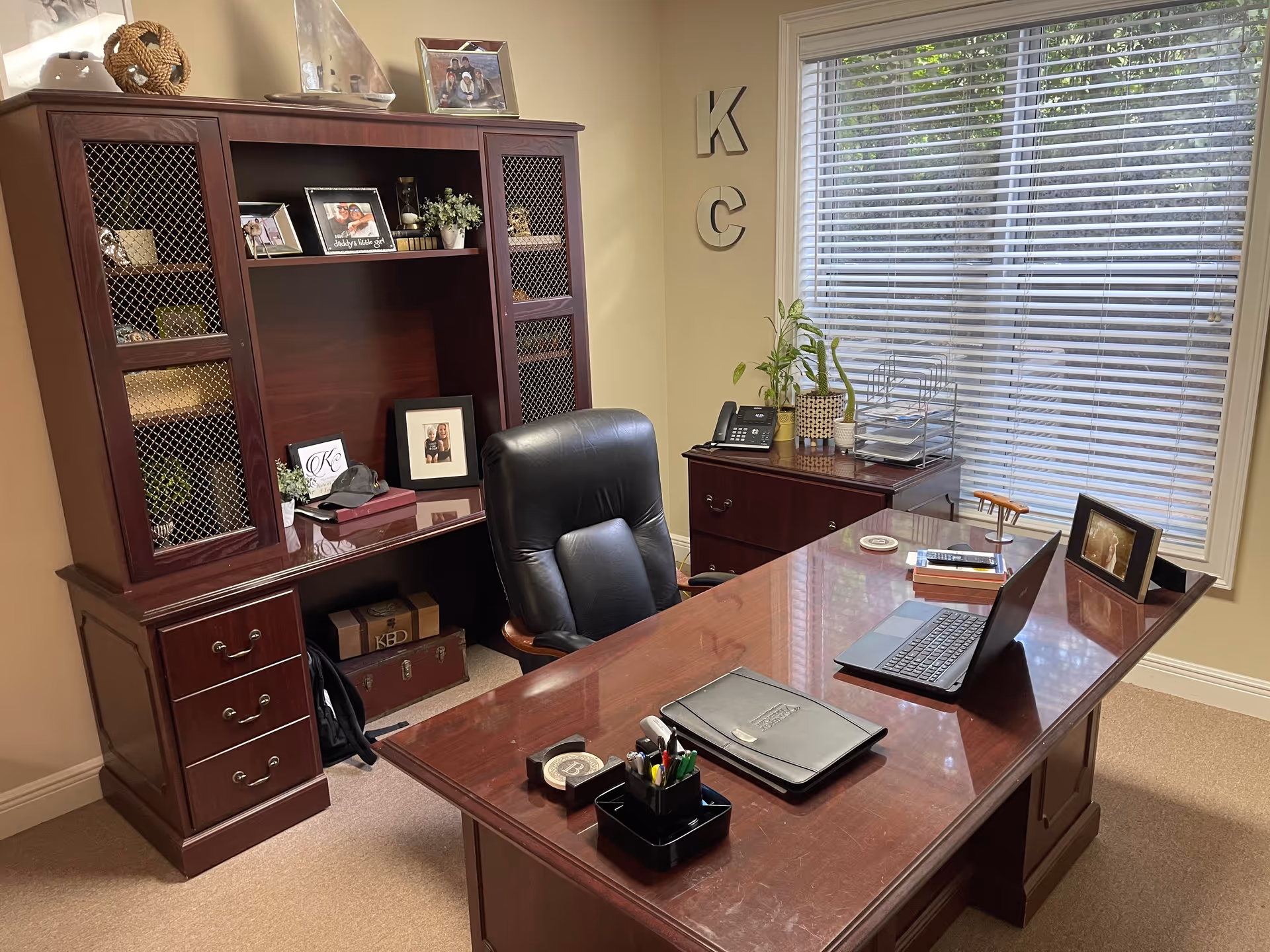 Executive-style mahogany desk with laptop, chair, and filing cabinet in office.