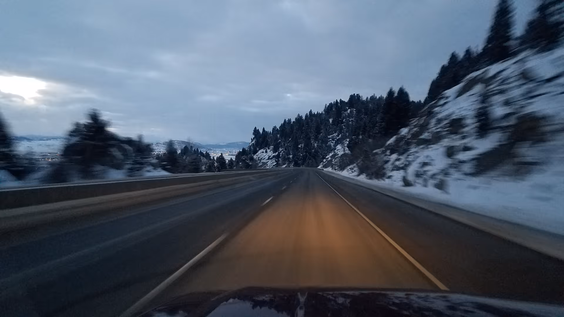Snowy mountain highway seen from a moving vehicle, with guardrails and snow-covered slopes.