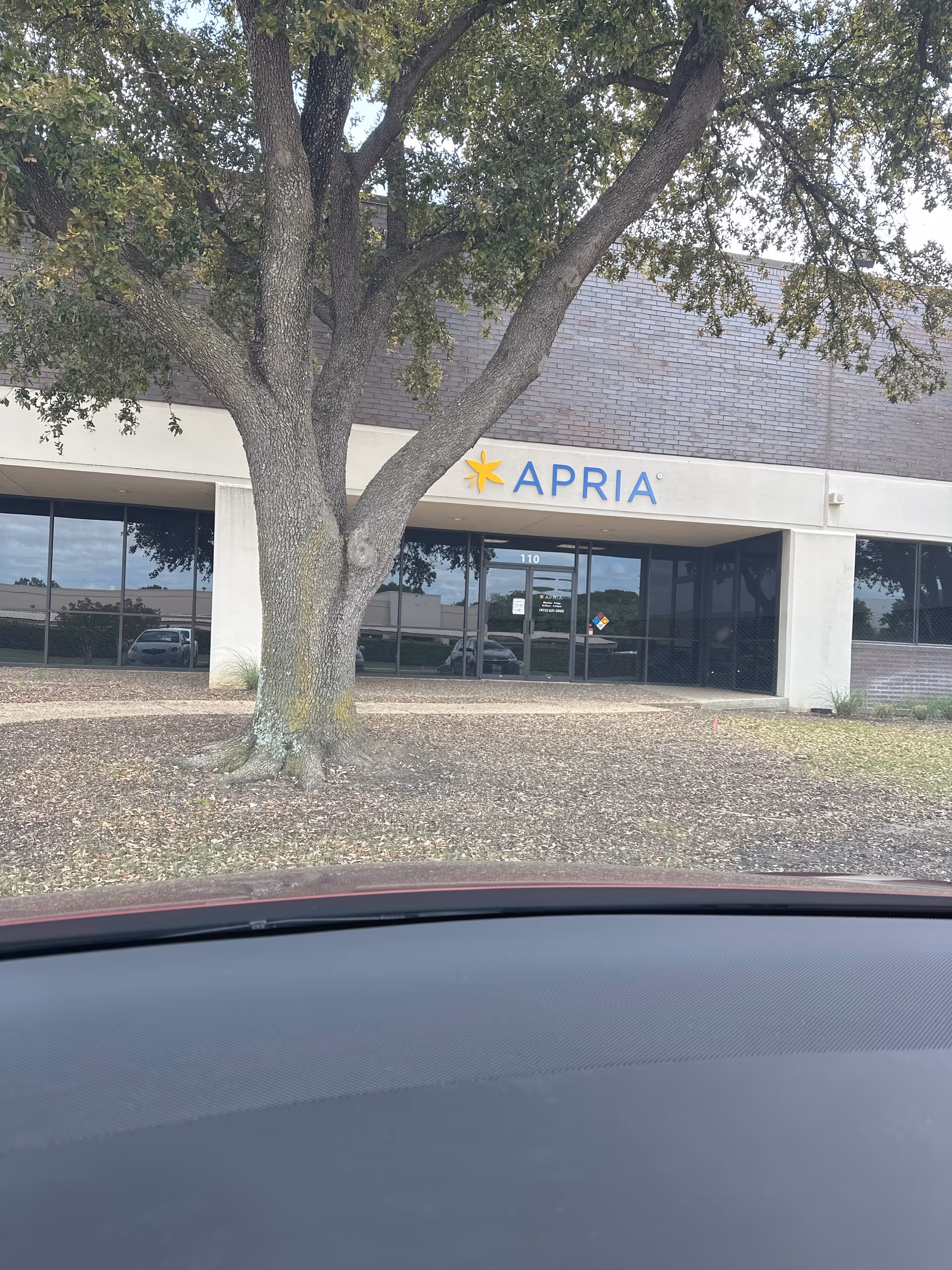 Exterior view of Apria Healthcare building entrance with a large tree.
