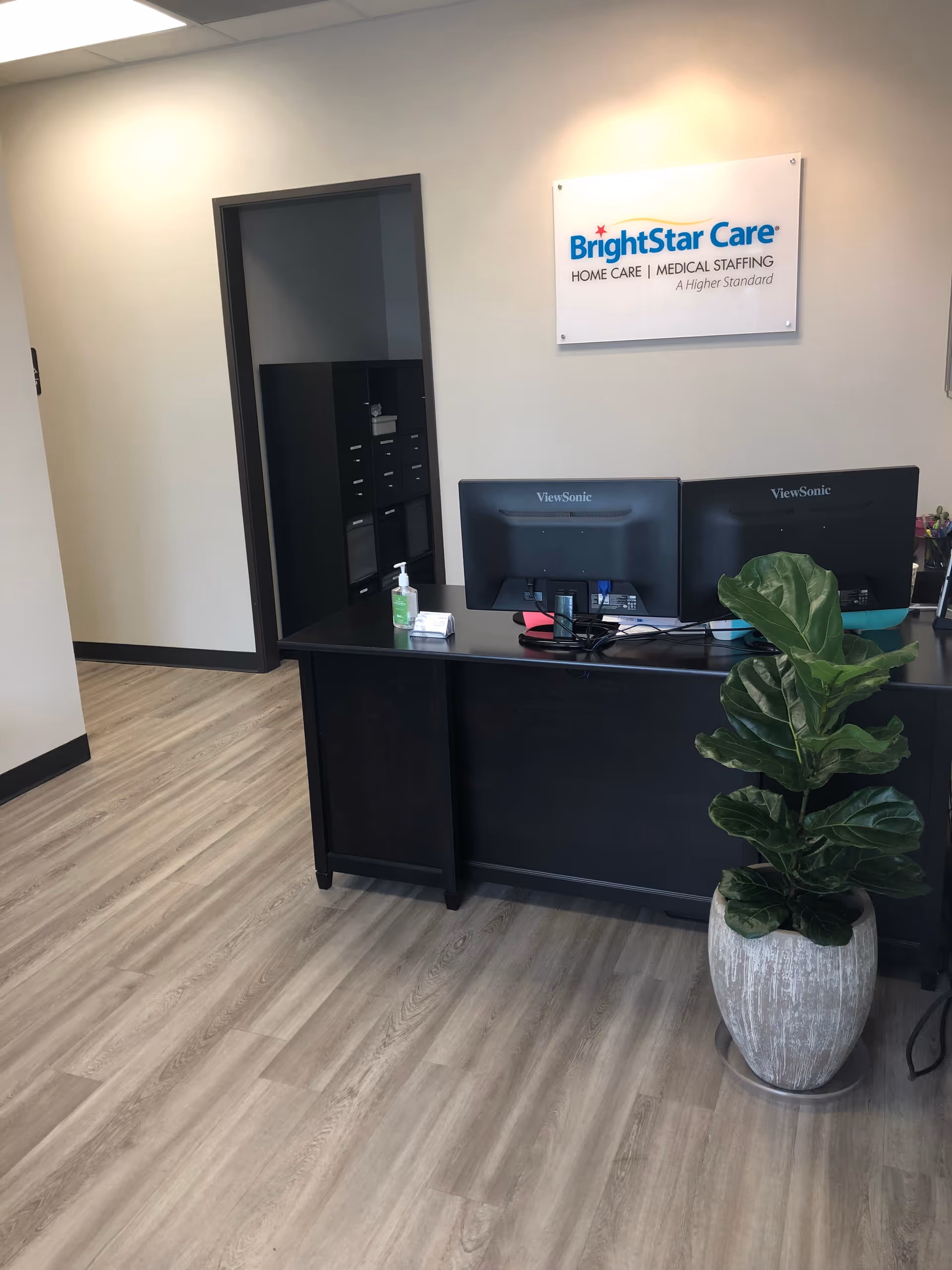 Reception desk with two monitors, sign, and a potted plant in BrightStar Care.