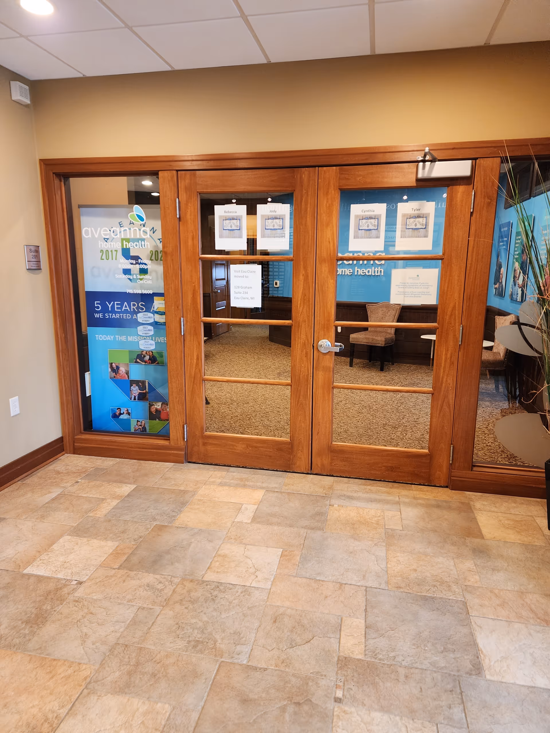 Wooden framed glass doors lead into a lobby area with Aveanna Home Health posters.