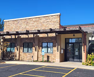 Exterior view of a single-story brick building with a covered entrance and parking.