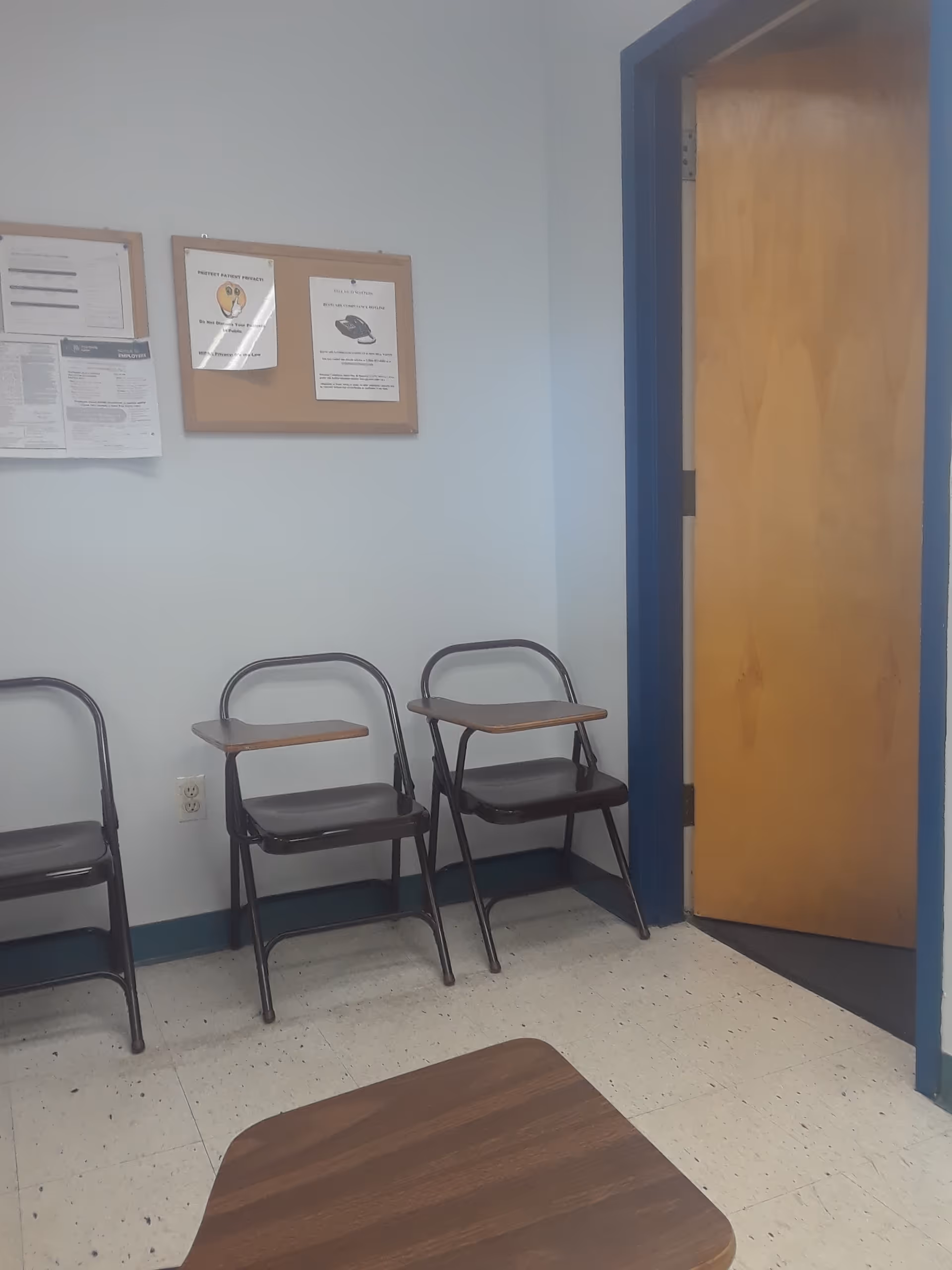 Small waiting area with metal chairs, a bulletin board, and a wooden table.