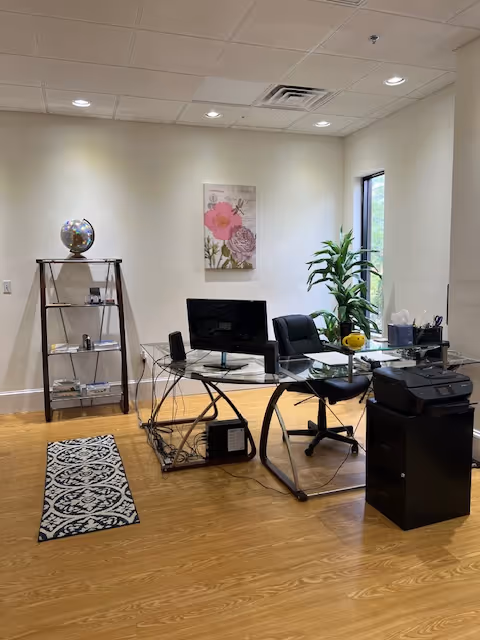 Modern glass desk office with computer, printer, plant, and wall art indoors.