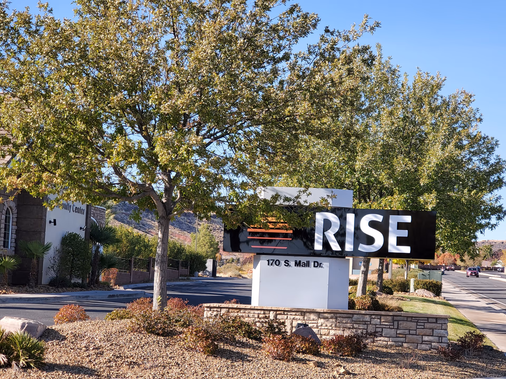 Outdoor entrance of RISE Services, Inc. with a large sign, trees, and landscaped surroundings.