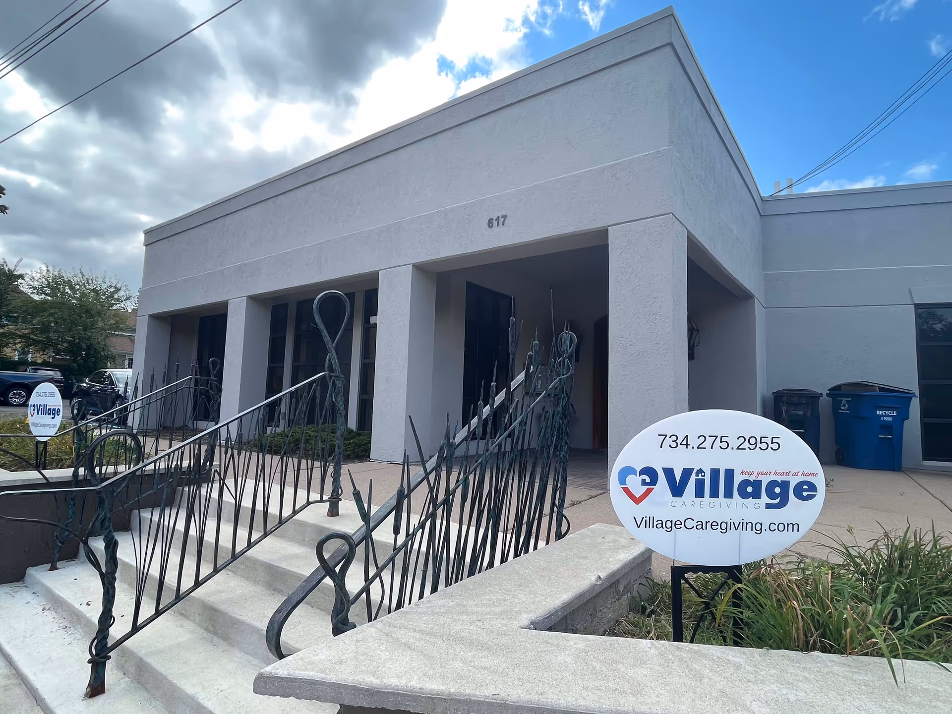 Front exterior of Village Caregiving building with entrance stairs and a round sign.